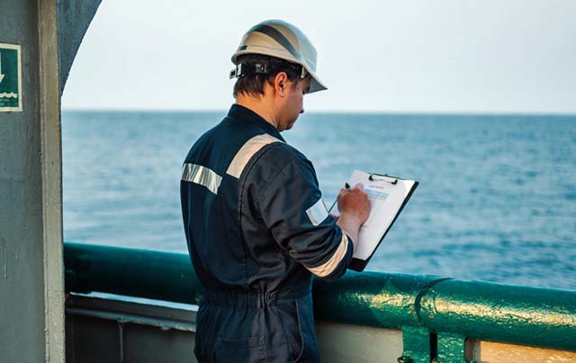 Deck Officer on deck of offshore vessel or ship , wearing PPE personal protective equipment. He fills checklist. Paperwork at sea IMO seafarer training (IMO)